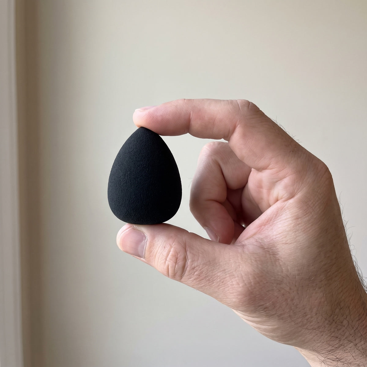 A man's hand holding the small black blending sponge